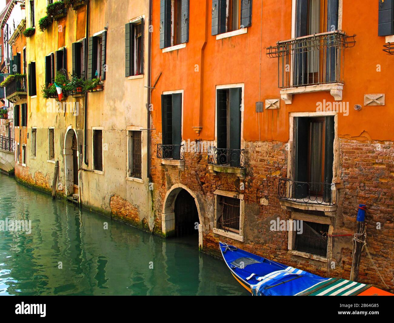 Canal street of Venice with orange painted houses and venetian boat tied to old building. Italy Stock Photo