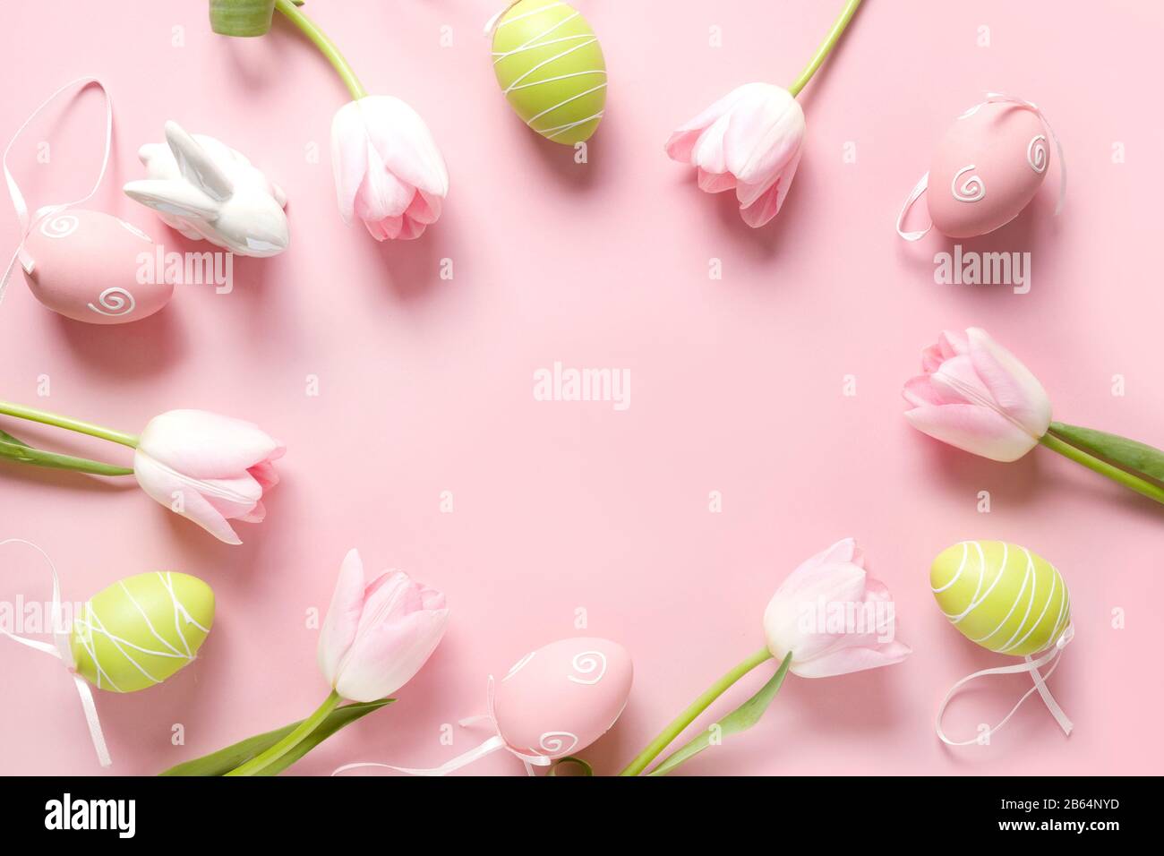 Easter frame of fresh pink flowers, bunny, colorful eggs and bunny on pink. Top view with copy space. Happy Easter holiday. Greeting card. Stock Photo