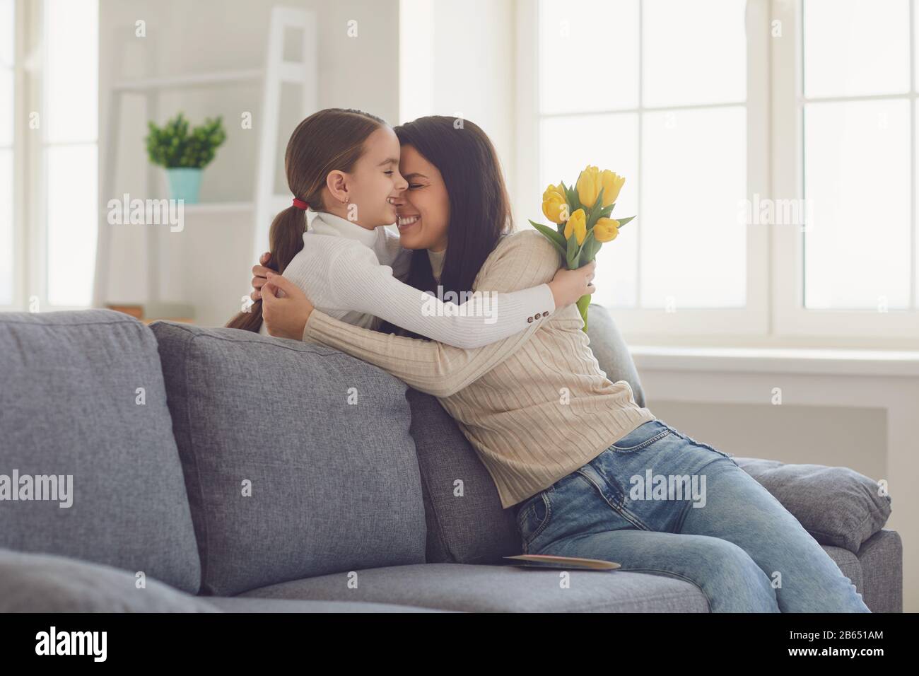 Happy mothers day. Daughter congratulates hugs his mother holds a bouquet of flowers in the room. Stock Photo