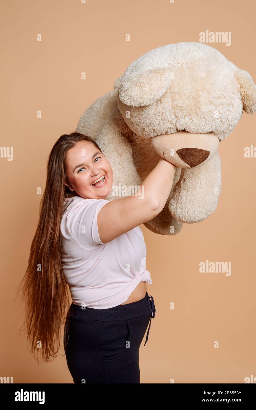 Overweight girl playing with a huge Teddy bear on a beige color Stock Photo