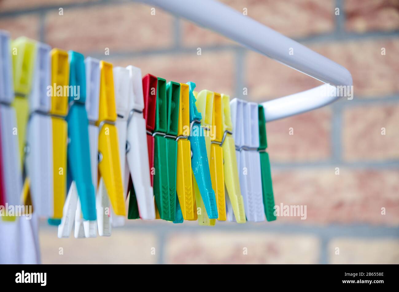 Colourful clothes pegs on a clothes horse against red brick wall Stock