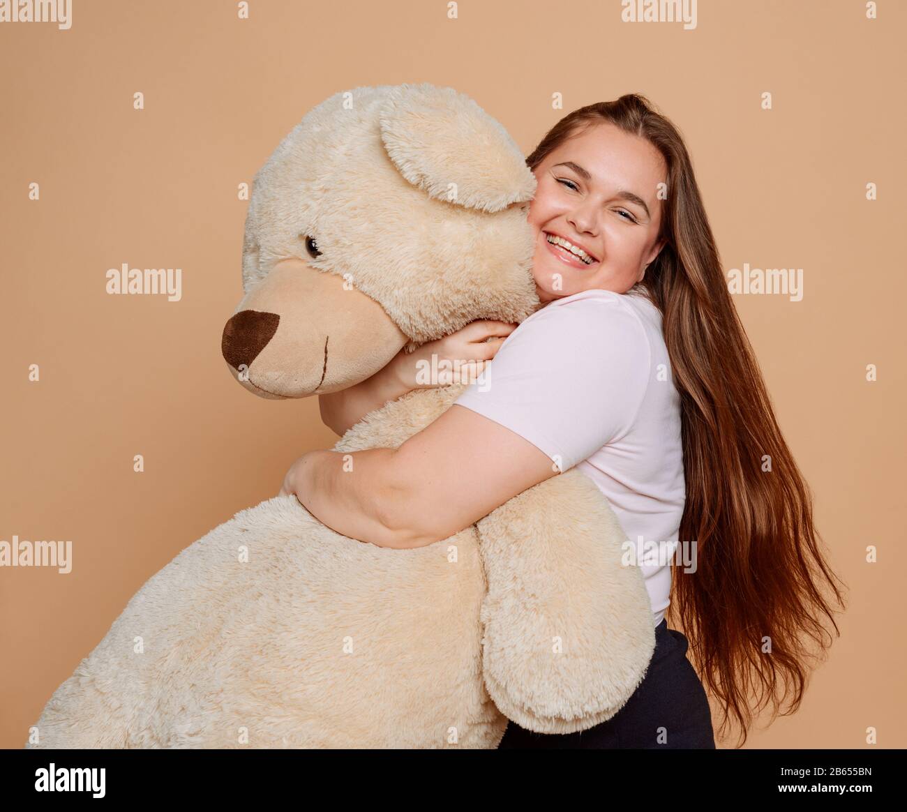 Grown woman hugging a huge Teddy bear on beige background Stock Photo