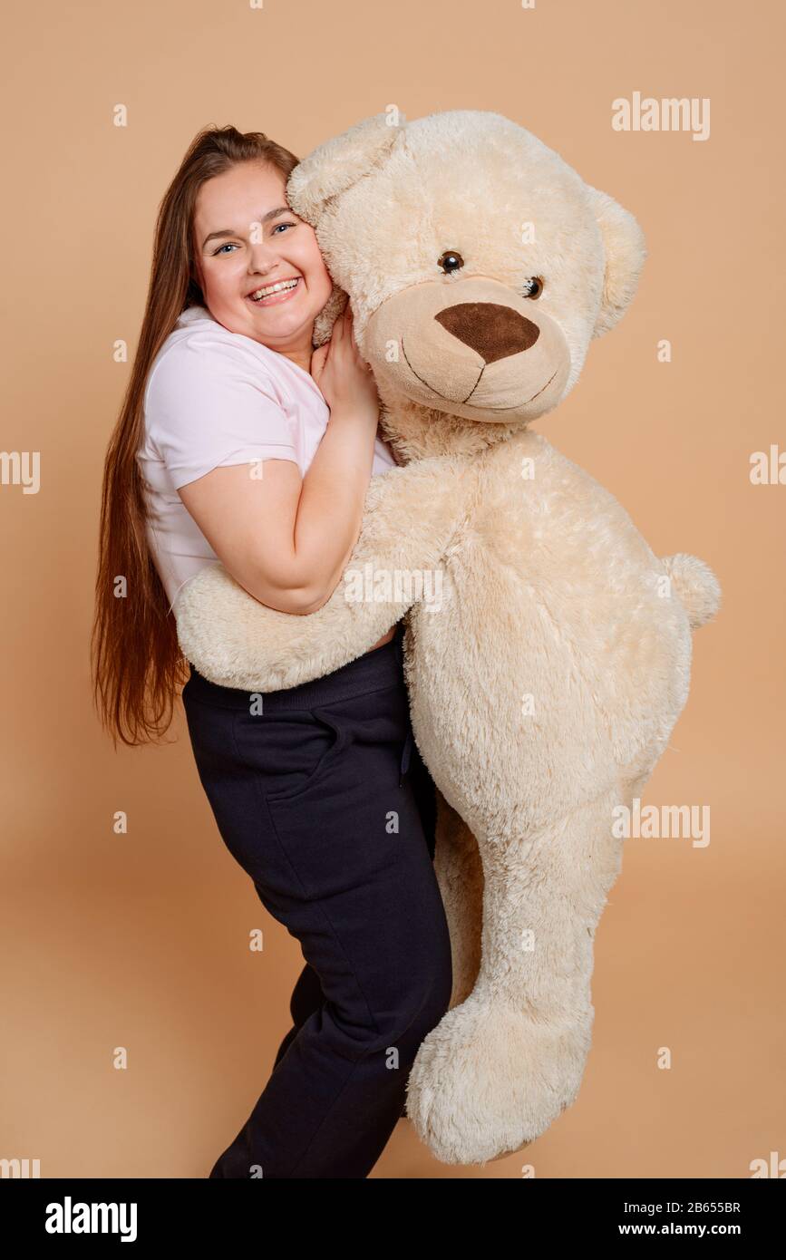 Plus size girl hugging a Teddy bear on beige background Stock Photo