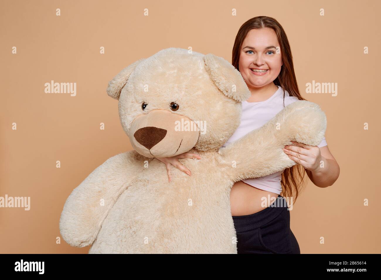Overweight woman hugging a huge Teddy bear on beige background Stock Photo
