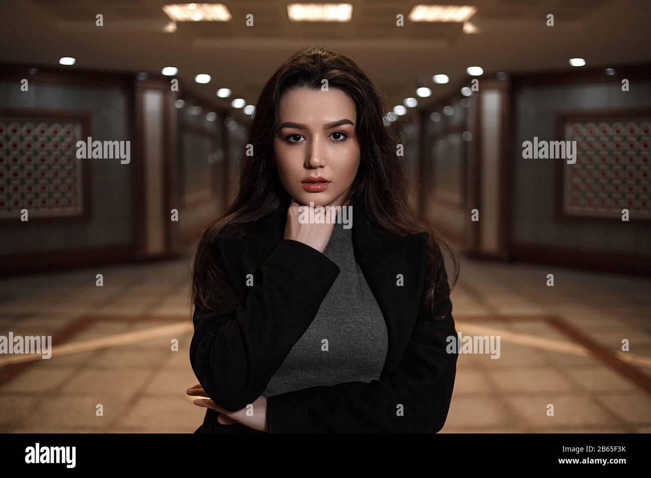 dramatic portrait of a beautiful young woman in a black coat in an underground passage.mosaics on the walls are not someone's works of art.these are w Stock Photo