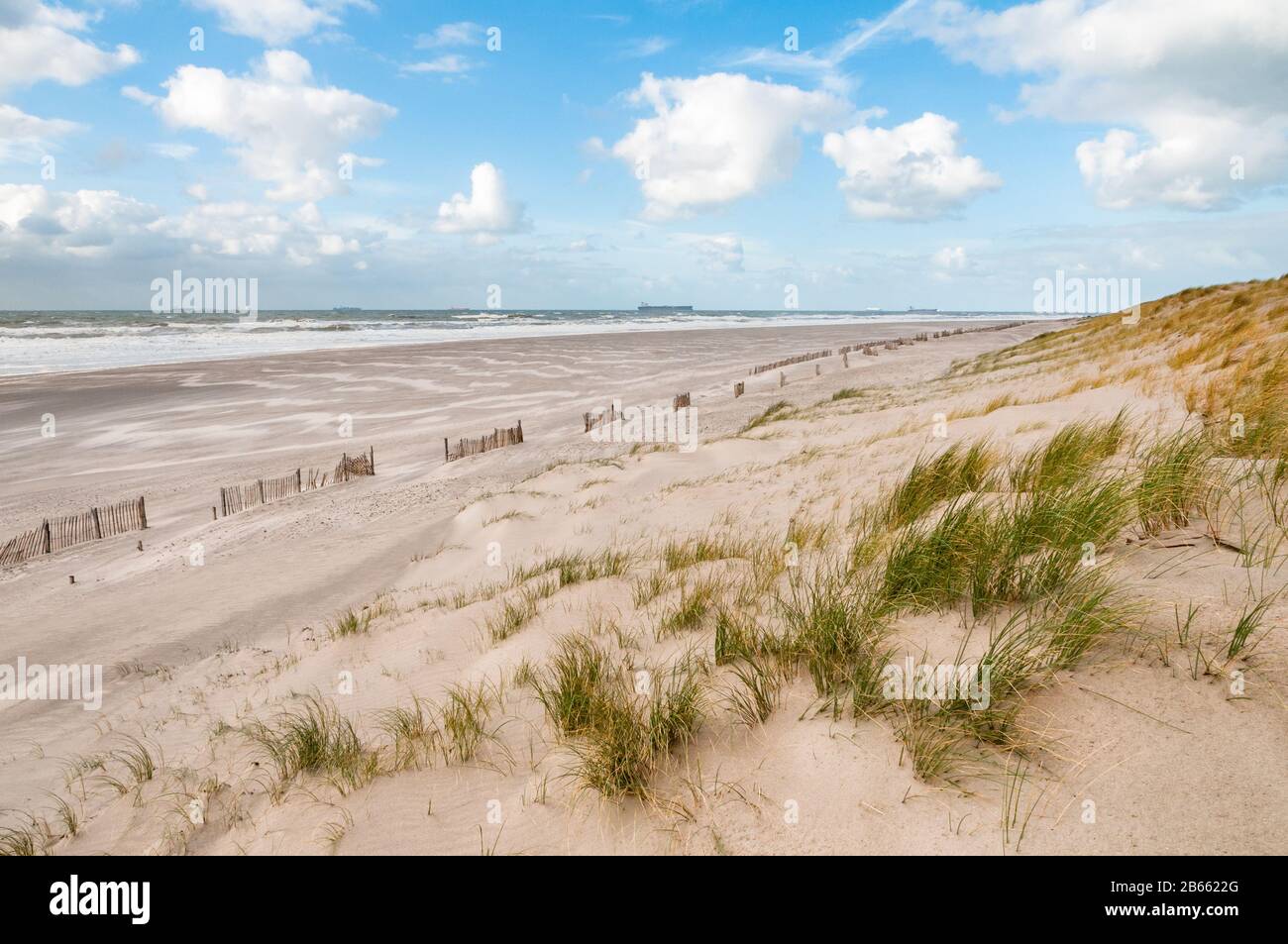 The beach and North Sea on a stormy but sunny day at the Maaslvakte near Rotterdam in the Netherlands. Ships arriving at the Port of Rotterdam in the Stock Photo