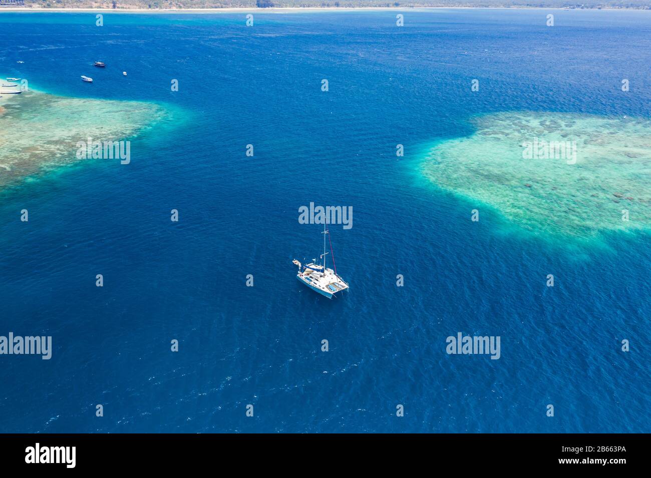 Aerial view of a sailboat next to a large, offshore tropical coral reef Stock Photo