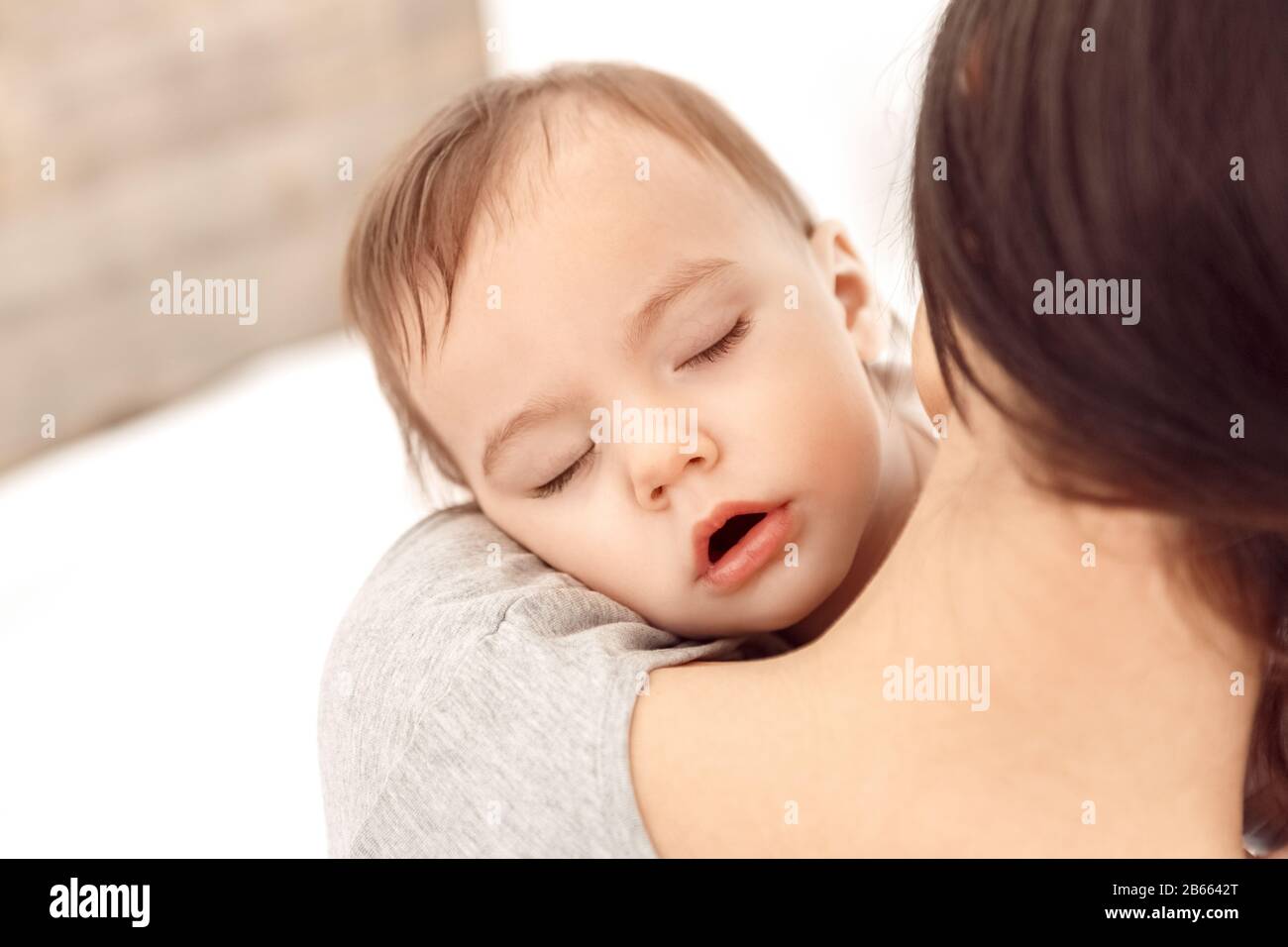 Motherhood. Mother holding adorable sleeping baby close-up at home back view Stock Photo