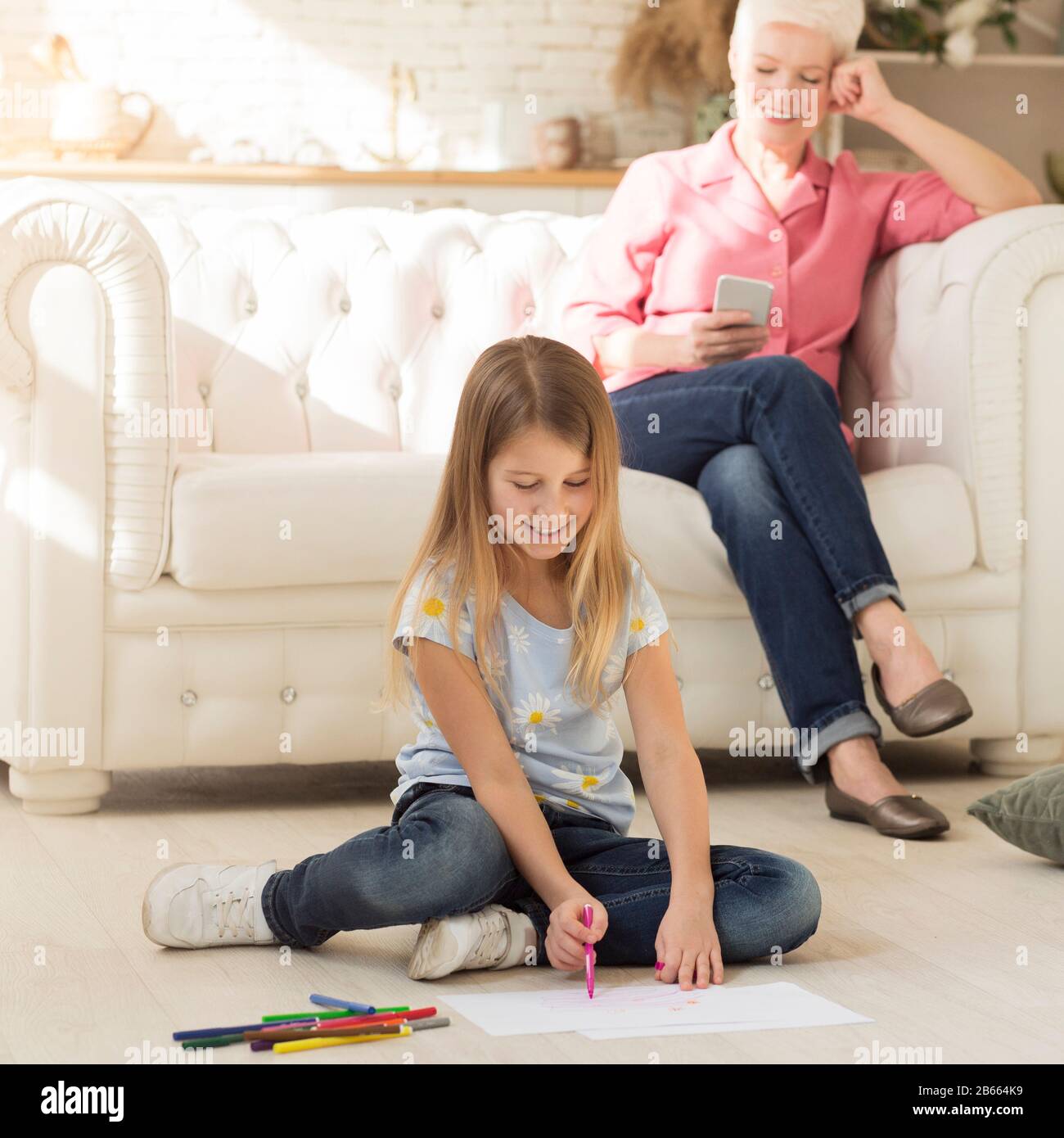 Little girl drawing on floor next to her granny Stock Photo