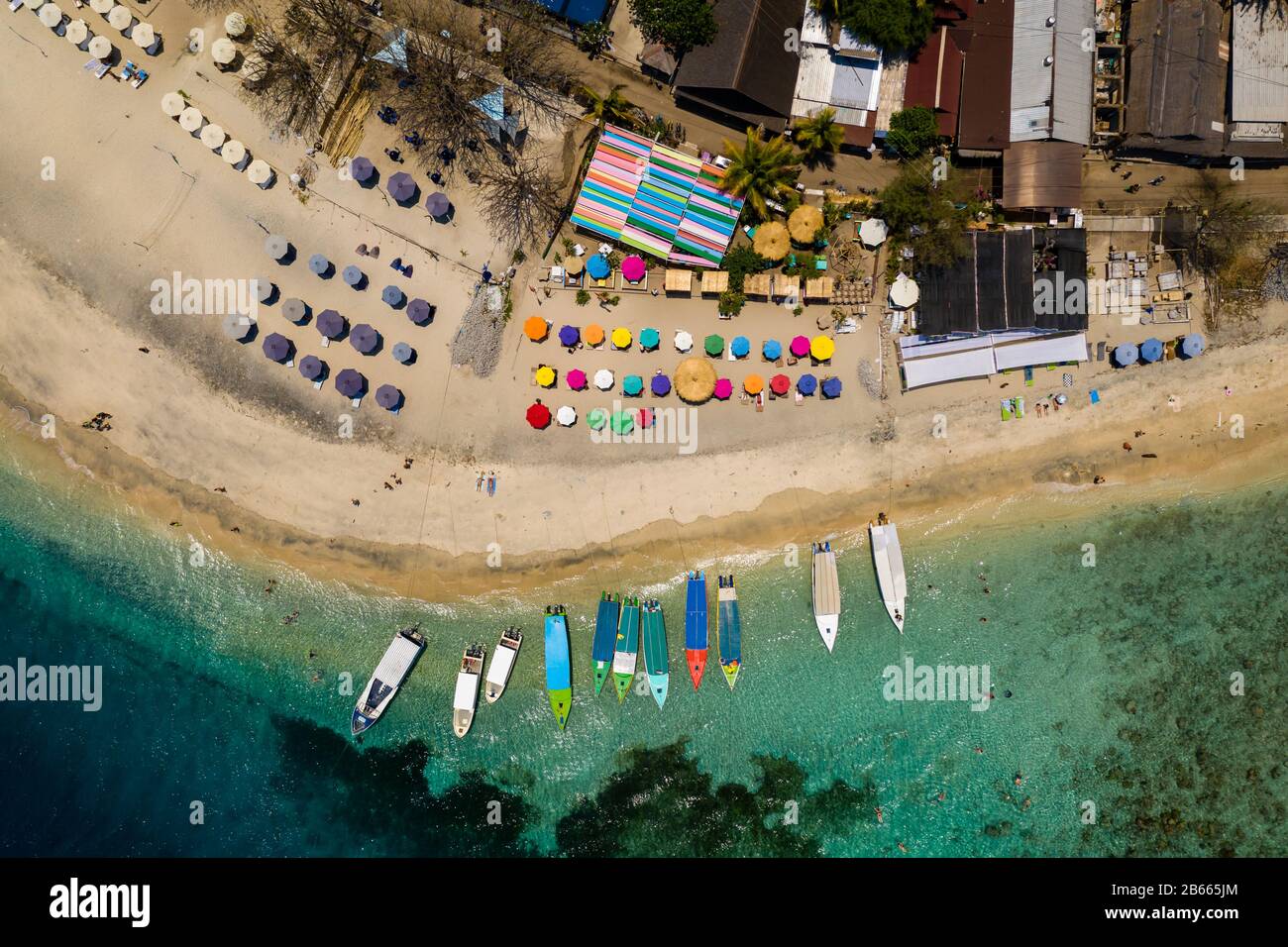 Top down aerial view of colorful boats and sunshades on a tropical beach on a small island fringed by a coral reef Stock Photo