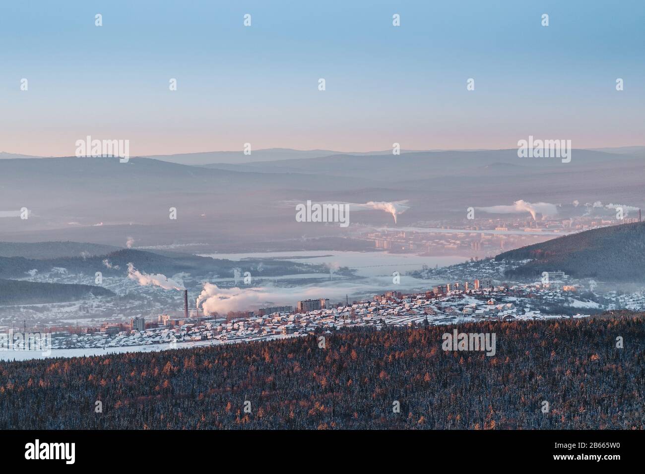 The aerial view of the industrial center of the Urals city of Zlatoust with the pipe smoke from the factories, surrounded by winter mountains. Stock Photo