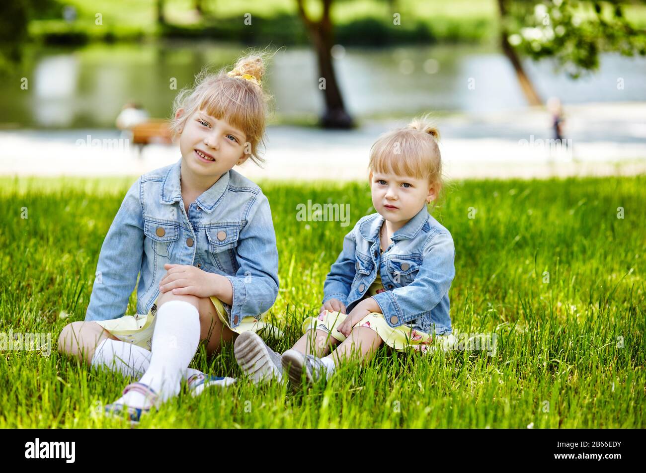 Adorable childs in blue trendy denim jaket posing outdoors. Girls having fun together. Little baby girls in the park. Summer or spring vacation Stock Photo