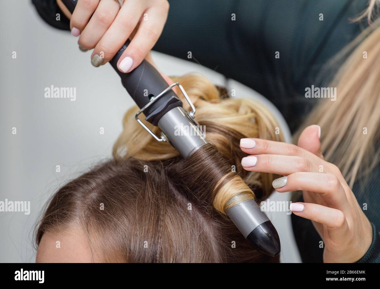stylist making ringlets to brunette woman. Hairdresser working with beautiful woman hair in hairdressing salon Stock Photo