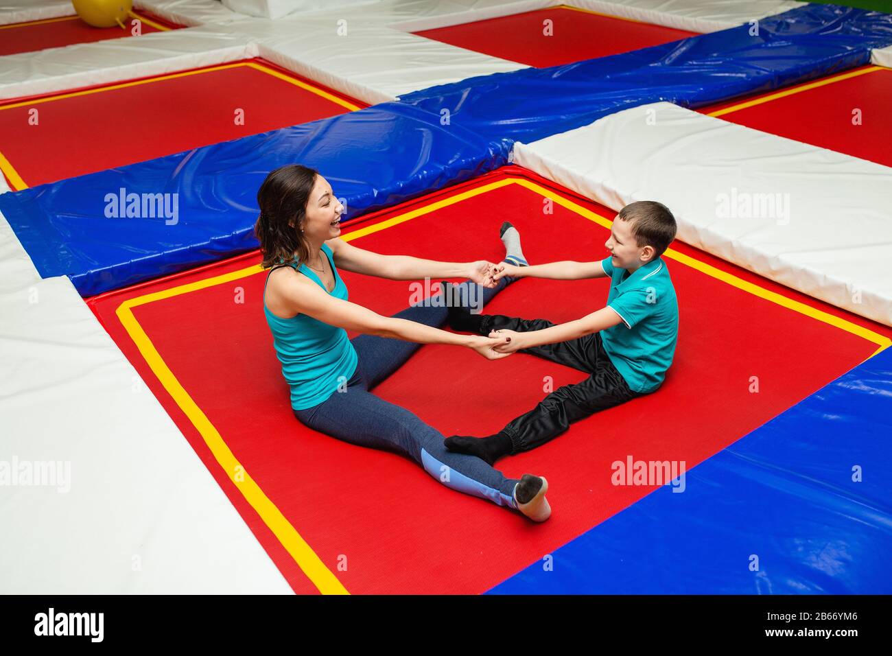 Mom with son is stretching on the floor on mats in the fitness gym and