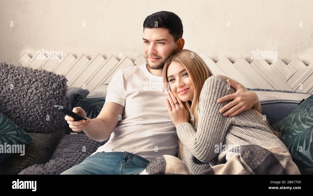 Attractive young woman and handsome man watching TV and hugging at home ...