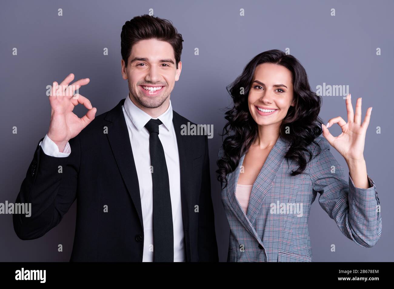 Portrait of beautiful two bussinesspeople showing ok sign wearing stylish black jacket blazer tie isolated over gray background Stock Photo
