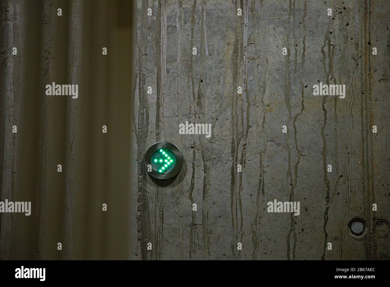 green arrow as directional sign in LED lights in a metal ring on a concrete wall Stock Photo