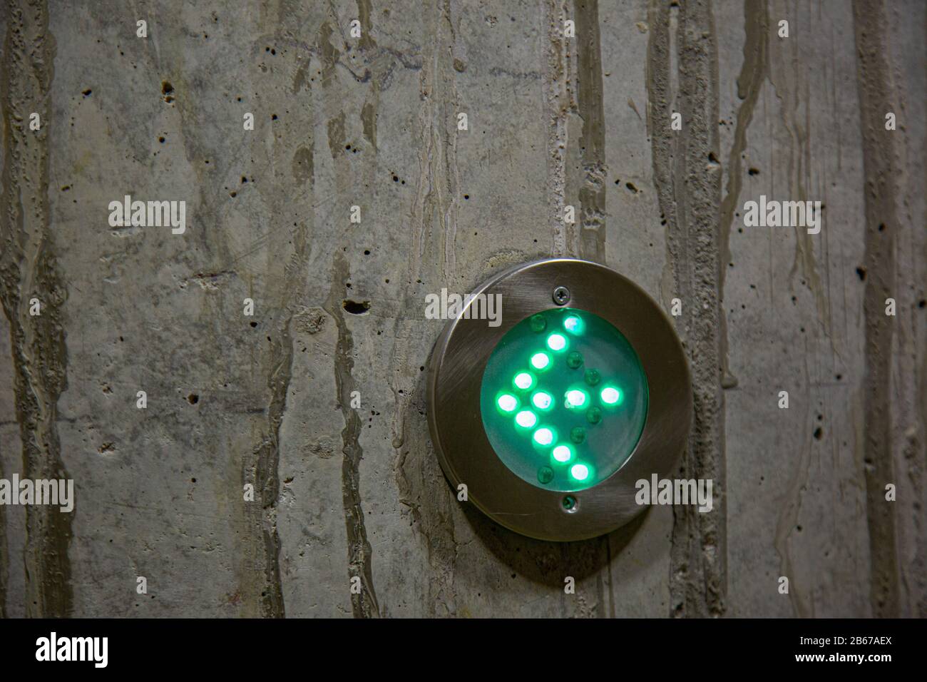 green arrow as directional sign in LED lights in a metal ring on a concrete wall Stock Photo