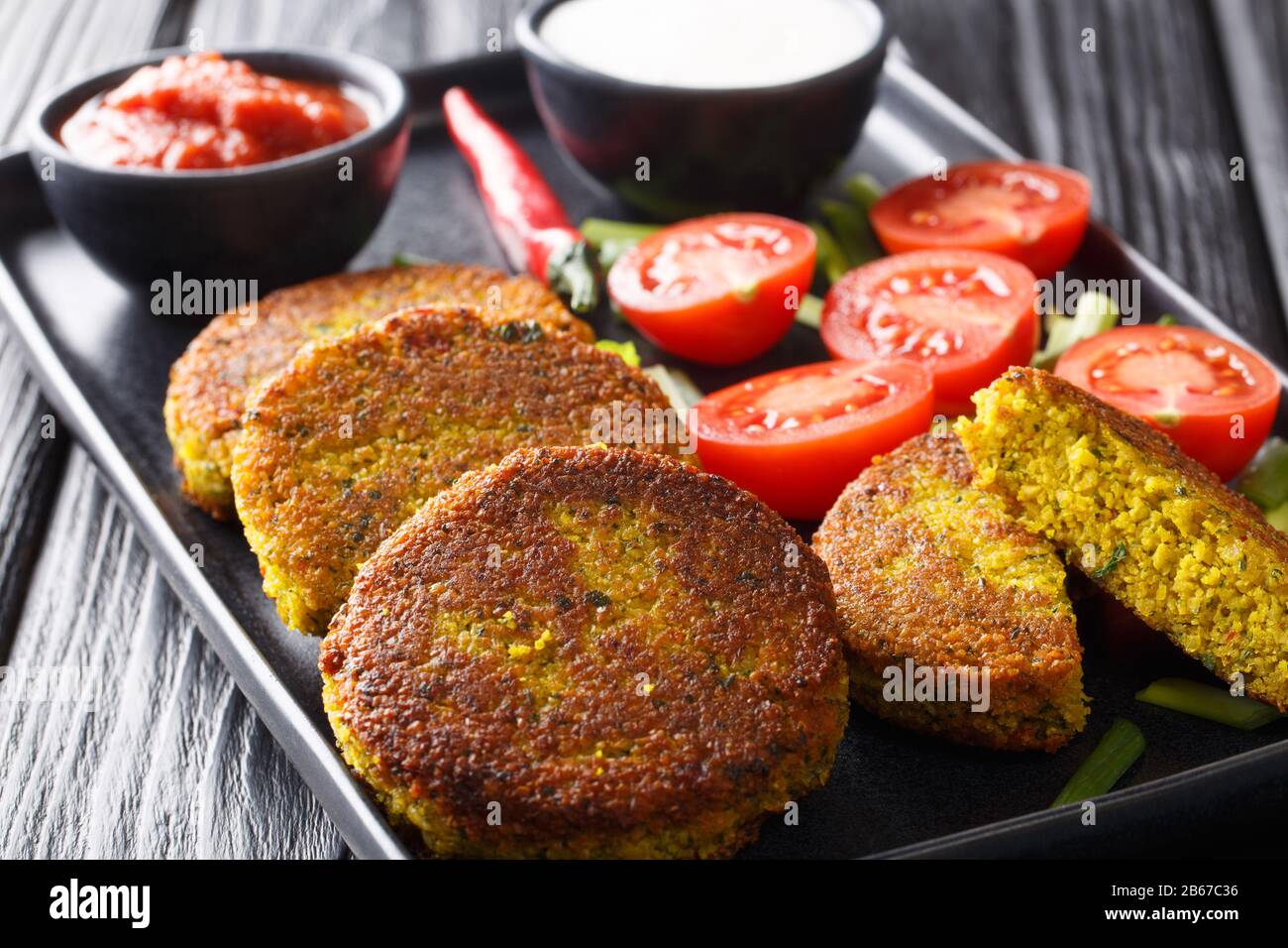 Yellow split pea fritters with fresh vegetables and sauces close-up in a plate on the table. horizontal Stock Photo