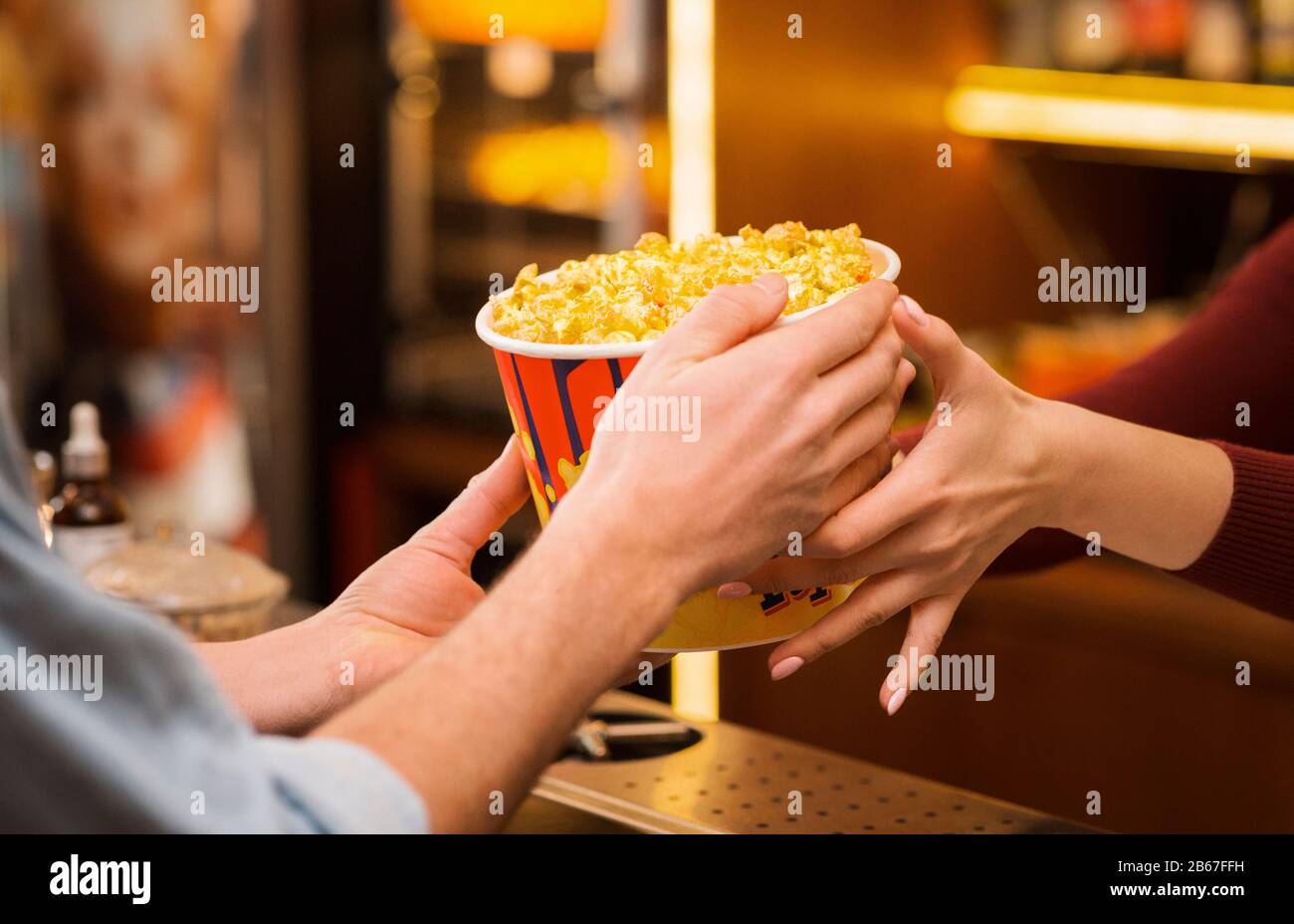 Young man buying popcorn from saleswoman in movie theater lobby, closeup of hands Stock Photo