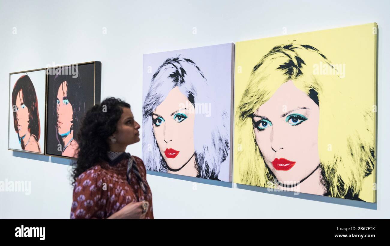 London, UK.  10 March 2020. A staff member poses next to (L to R) 'Mick Jagger' and 'Debbie Harry', 1980, both by Andy Warhol. Preview of 'Andy Warhol', a retrospective of over 100 works by one of the most recognisable artists of the late 20th century.  The exhibition runs 12 March to 6 September 2020 at Tate Modern. Credit: Stephen Chung / Alamy Live News Stock Photo
