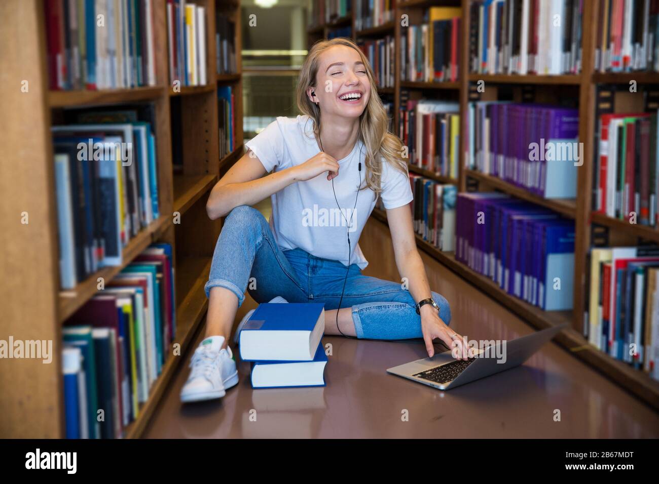 Young girl sitting on the floor in traditional library at bookshelves ...