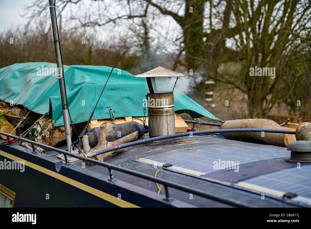 Smoke drifts out of a chimney on a narrowboat stacked with fuel while moored in Ellesmere, Shropshire. Stock Photo