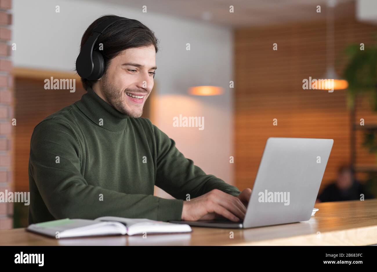 Young positive man in wireless headphones studying online on laptop Stock Photo