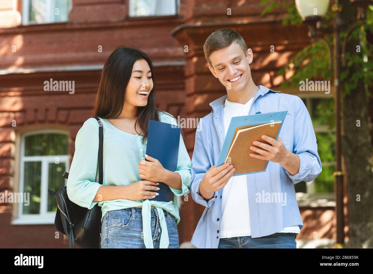 Student couple going to class, checking lessons schedule outdoors and laughing Stock Photo