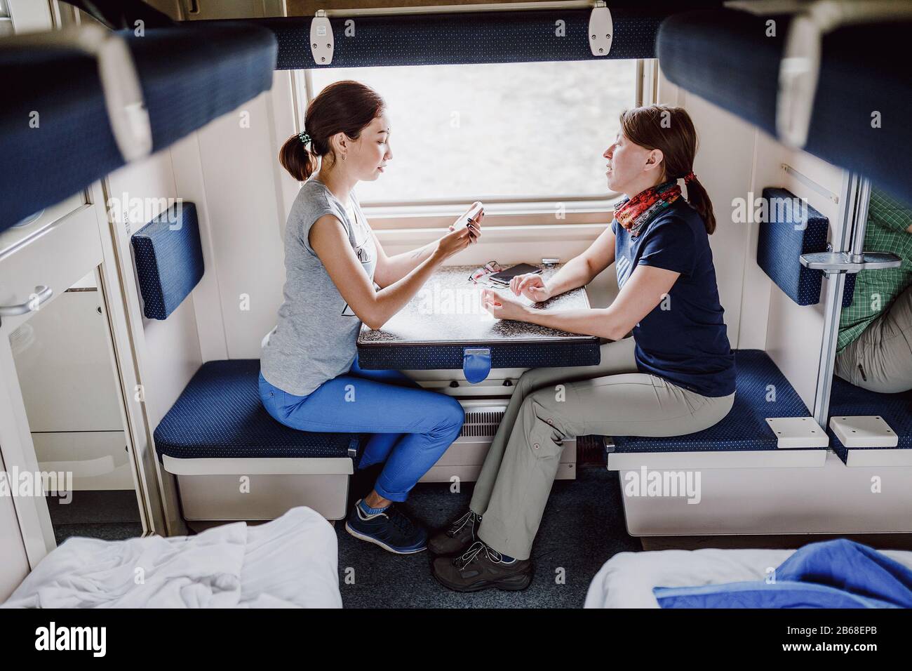 Two women Friends talking and laughing while traveling by reserved ticket train, railroad trip concept Stock Photo