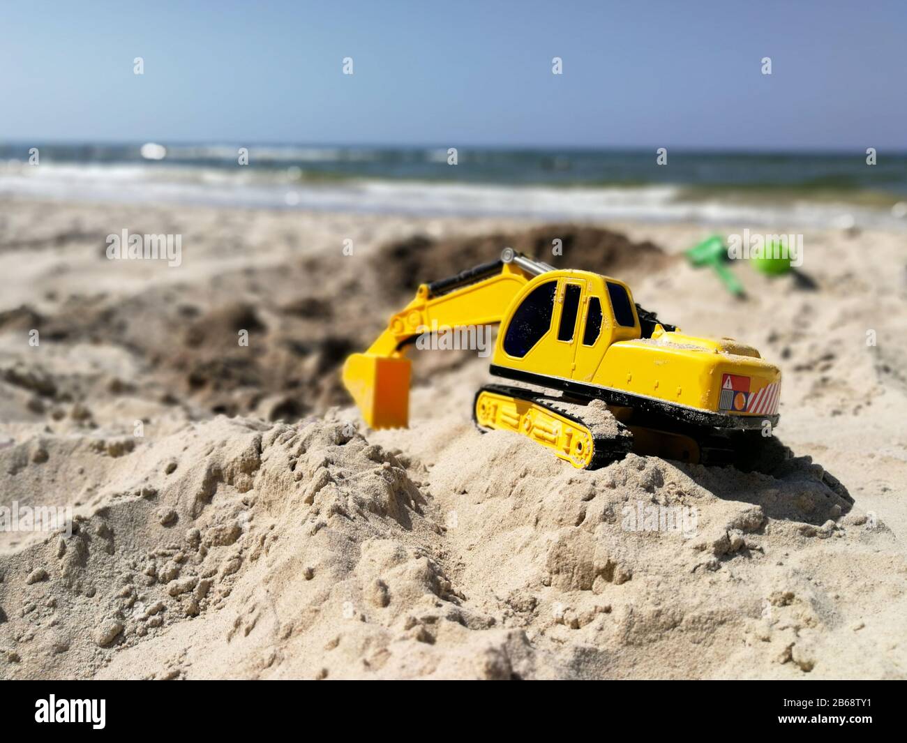 Plastic toy excavator prepared for digging hole on the sandy beach