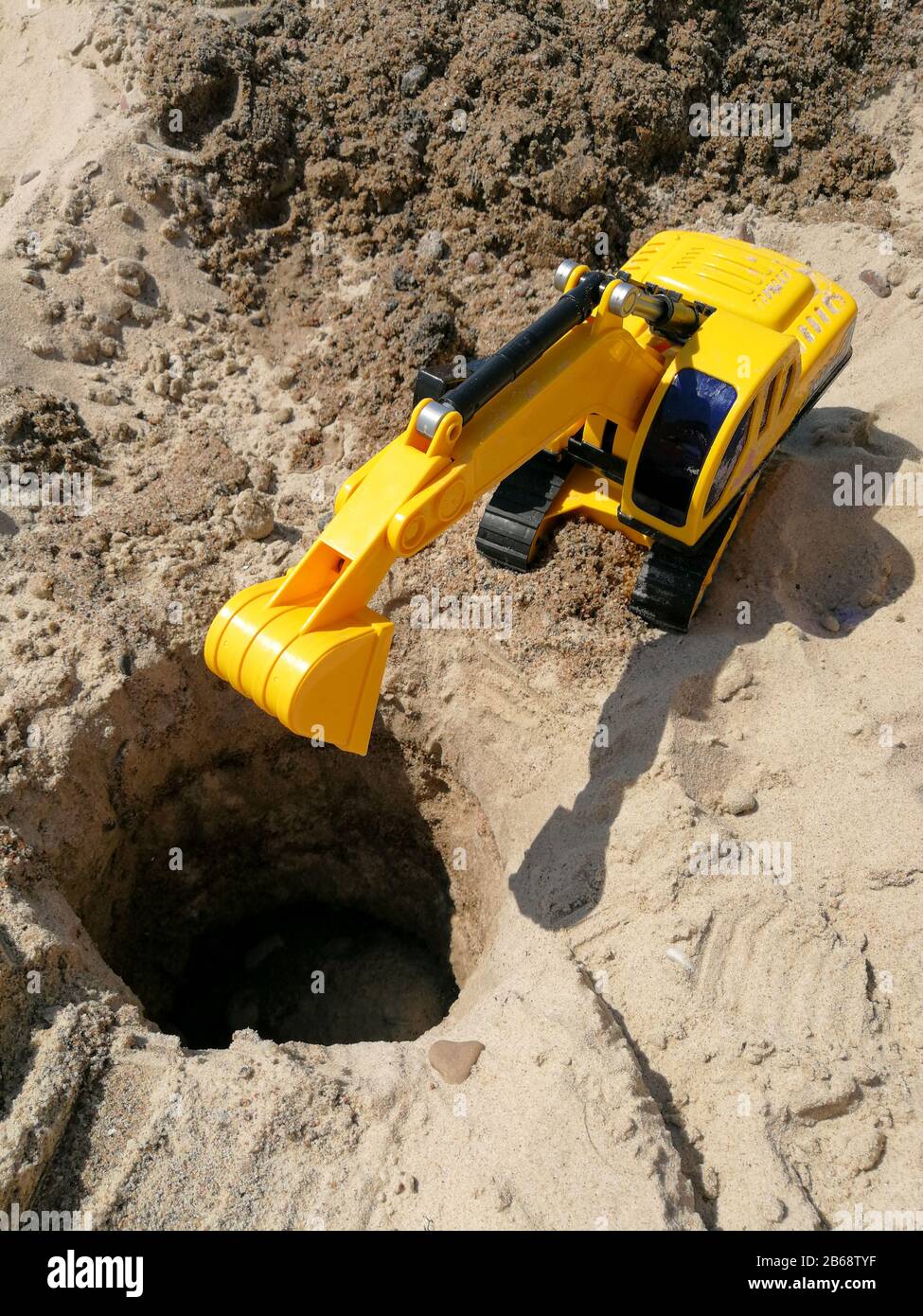 Plastic toy excavator prepared for digging hole on the sandy beach