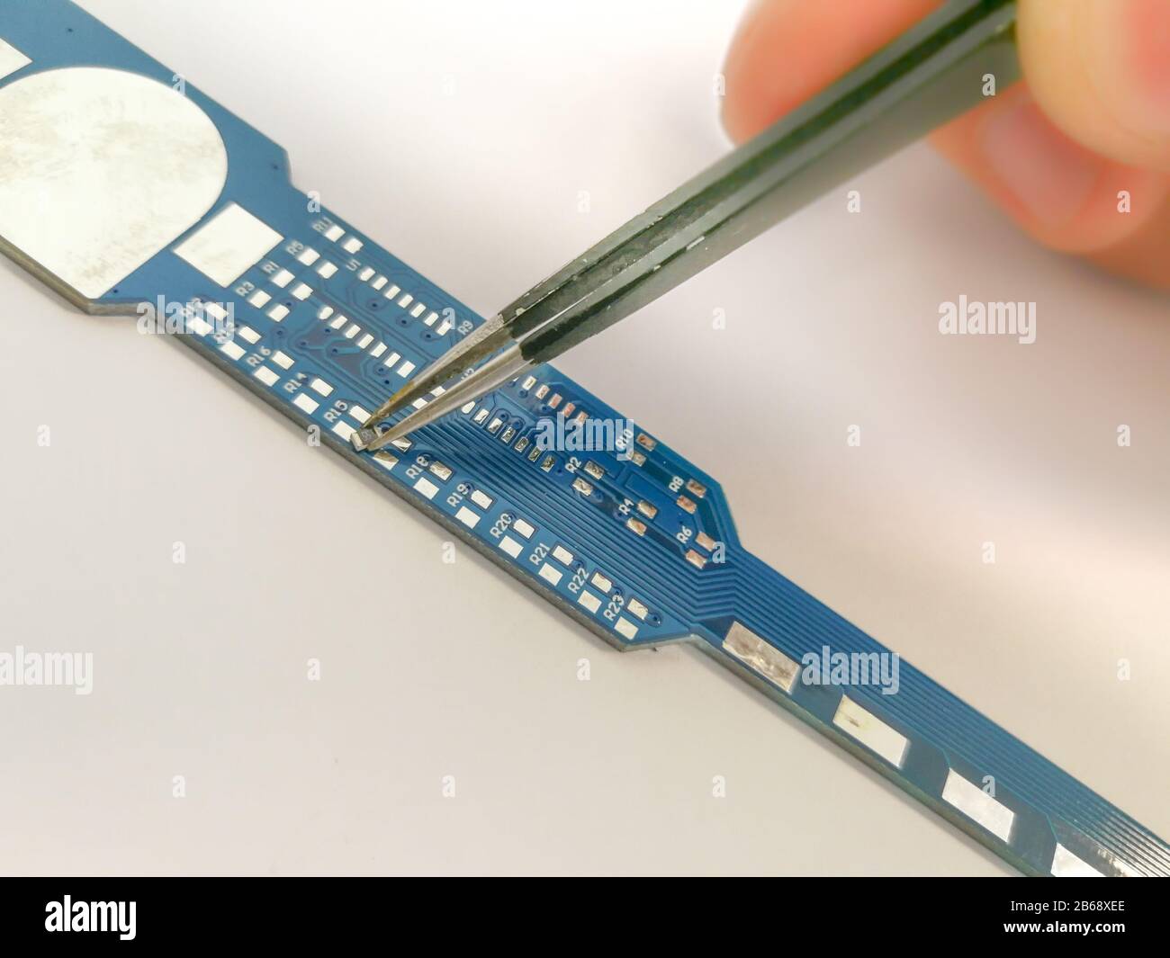 Manual PCB assembly process by hand. Male hand holding tweezers with