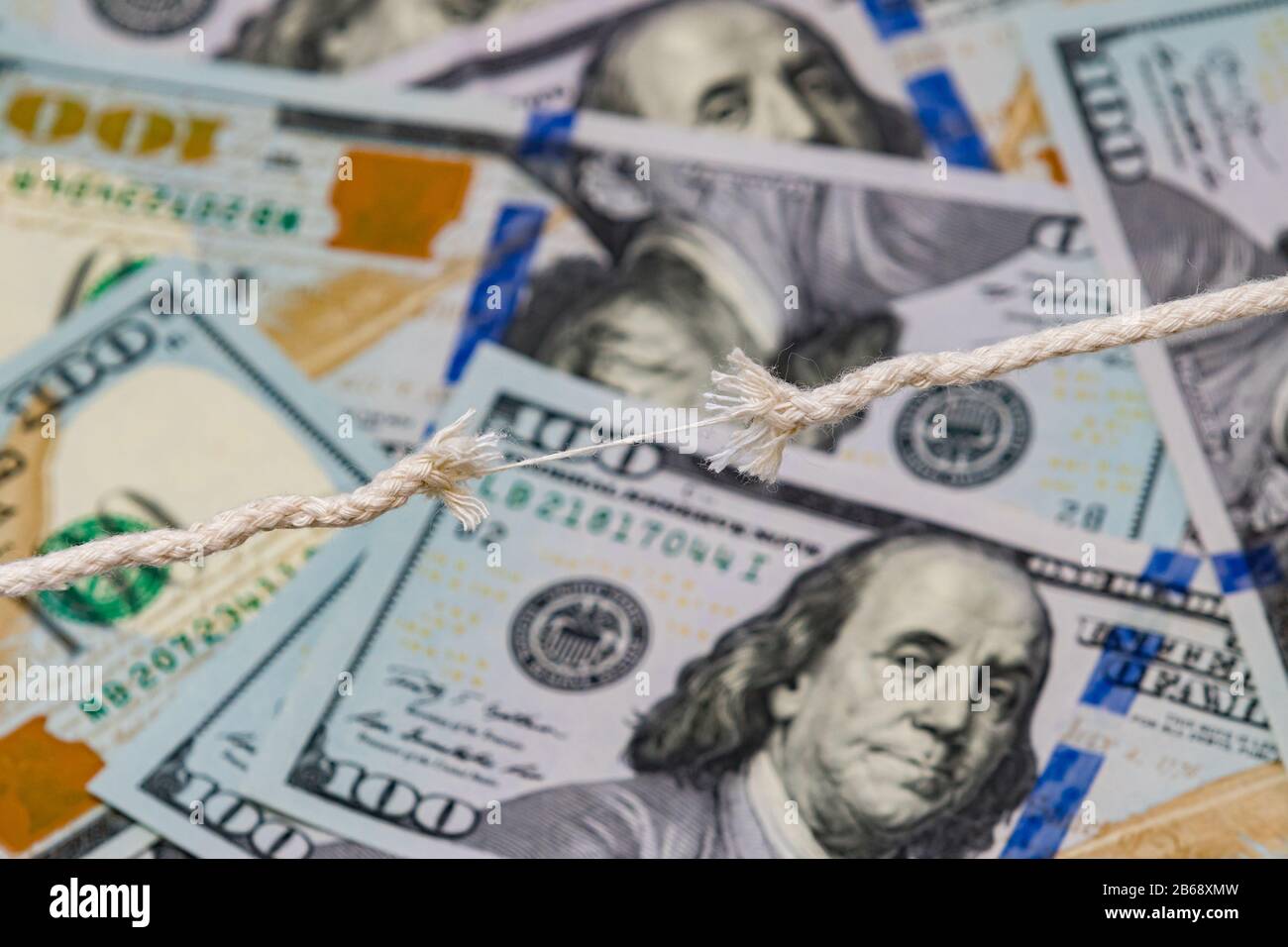 Closeup of frayed breaking rope with 100 dollar bills in background. Concept of fragile economy, stock market decline and crash, recession Stock Photo