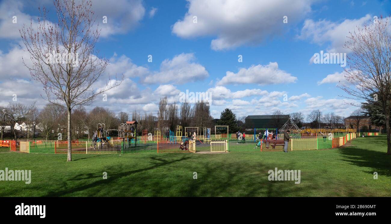 Children enjoying the play areas in Salt Hill Park, Slough, whilst their parents look on. Sunny day. Late winter. Stock Photo