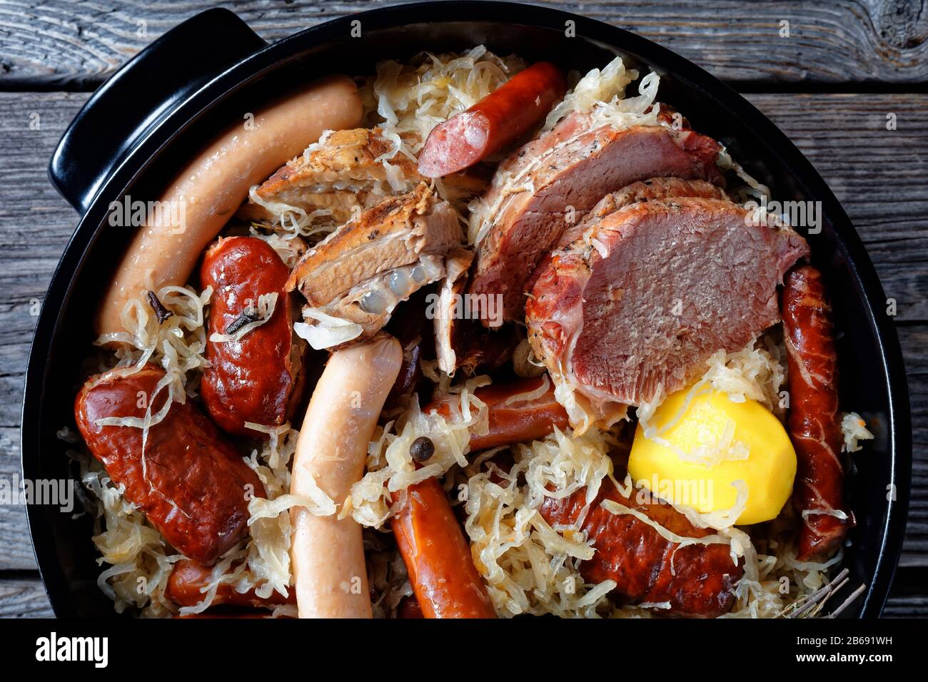Sour cabbage stew with different types of meat and sausages and potato stewed in white wine with onion thyme juniper berries, garlic served on a black Stock Photo