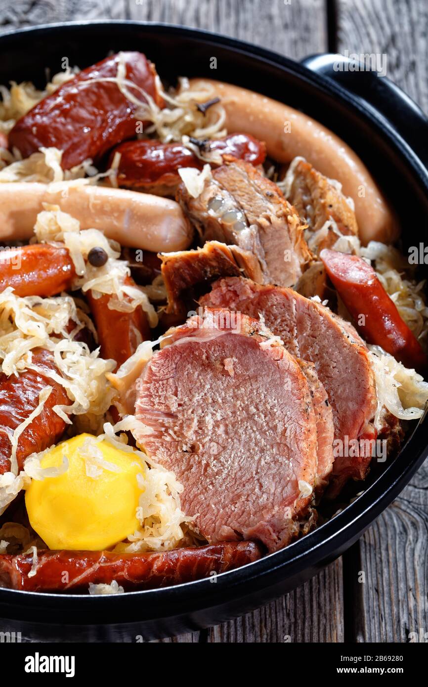 Сhoucroute garnie french stew of fermented cabbage with pork loin, bacon, and sausages cooked with potato in white wine, thyme, cloves on a black baki Stock Photo