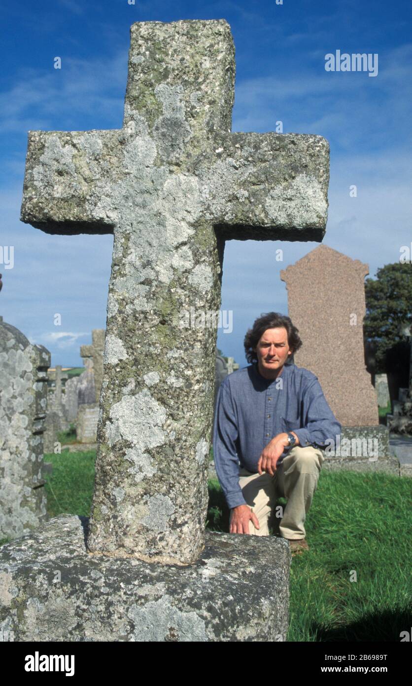 man kneeling by old stone cross in graveyard Stock Photo