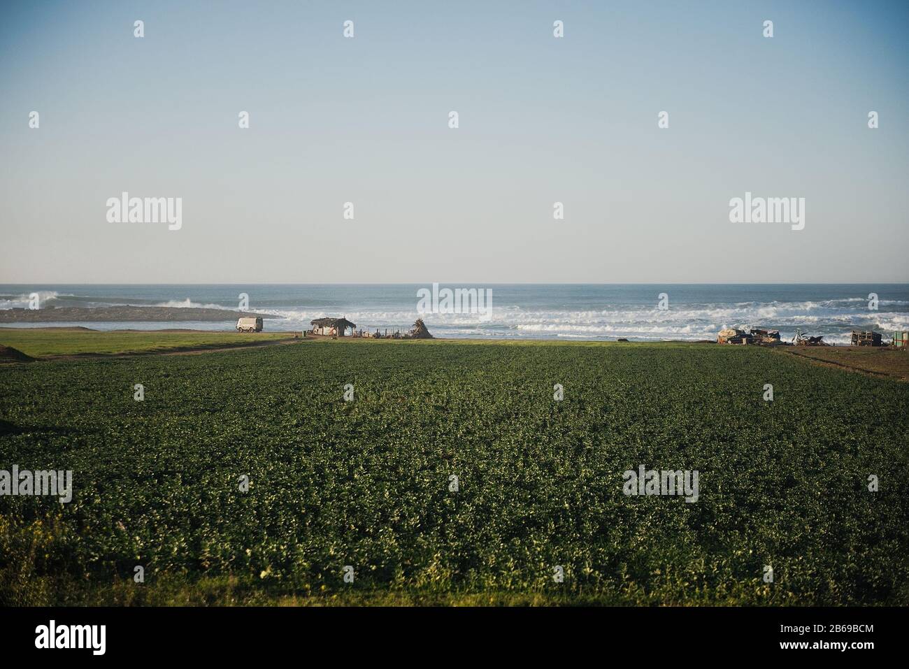 Colorful straw house on farmland with blue ocean, sea and coastline in the background. Stock Photo