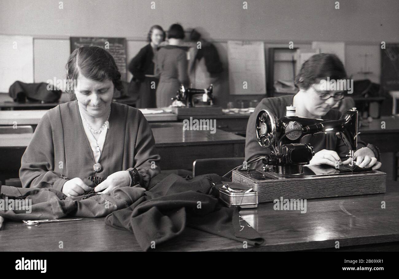 1940s, historical, post-war Britain, adult education.....two ladies sitting at a long desk in a classrom, in a sewing class, one using a sewing machine, the other hand sewing a piece of clothing, England, UK. The first Industrial Revolution saw the invention of machines to reduce the amount of manual sewing work by workers in clothing companies. Stock Photo