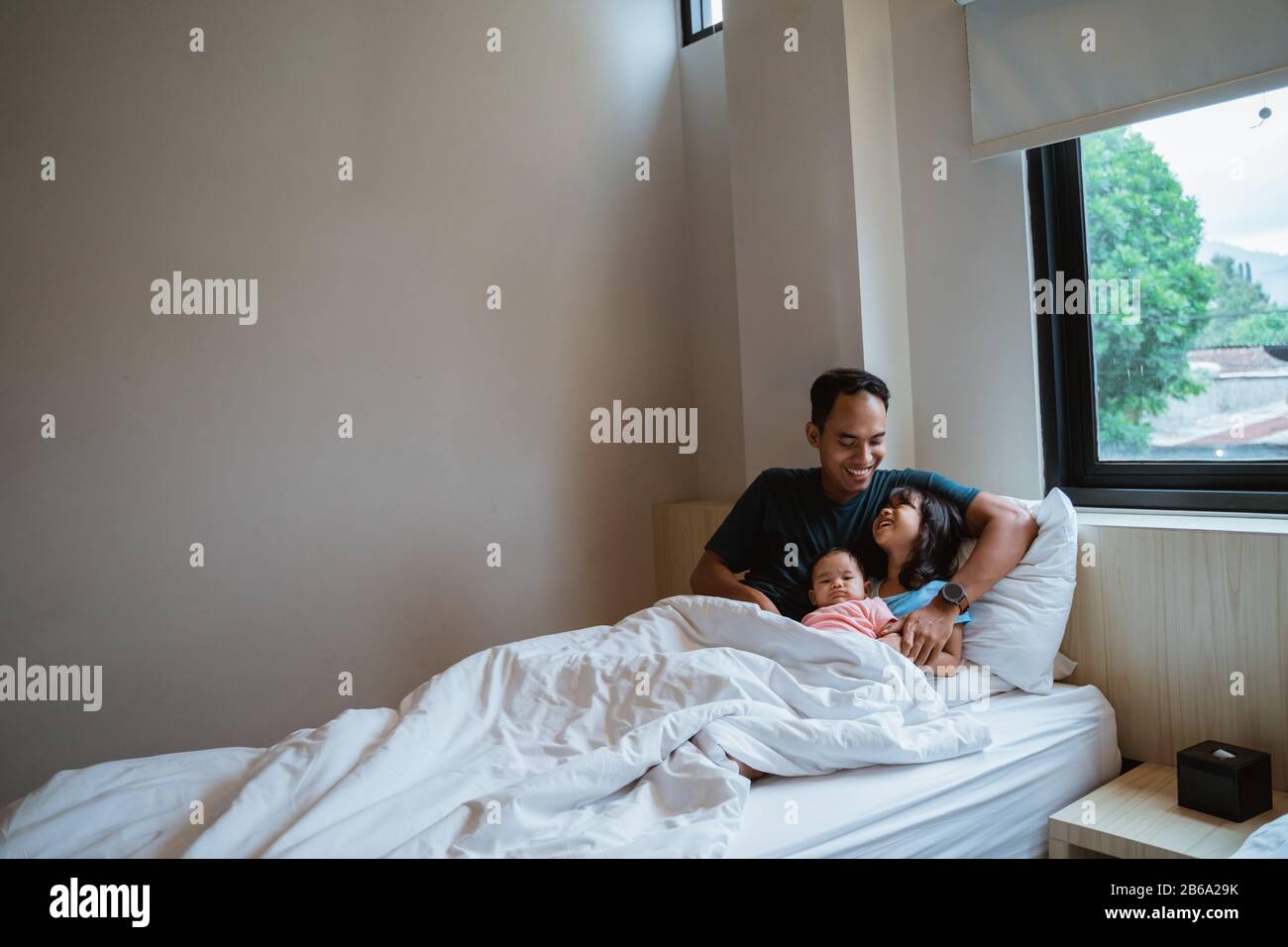 two daughters and their father sit on the bed when they wake up Stock