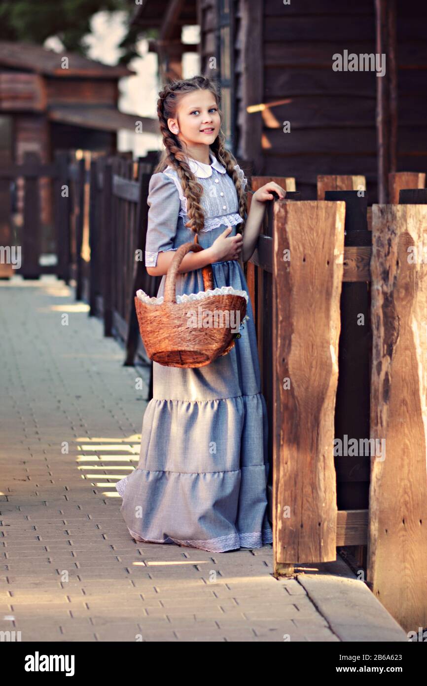 Girl with a basket in hands and in a retro dress on a background of a wooden rural house Stock Photo