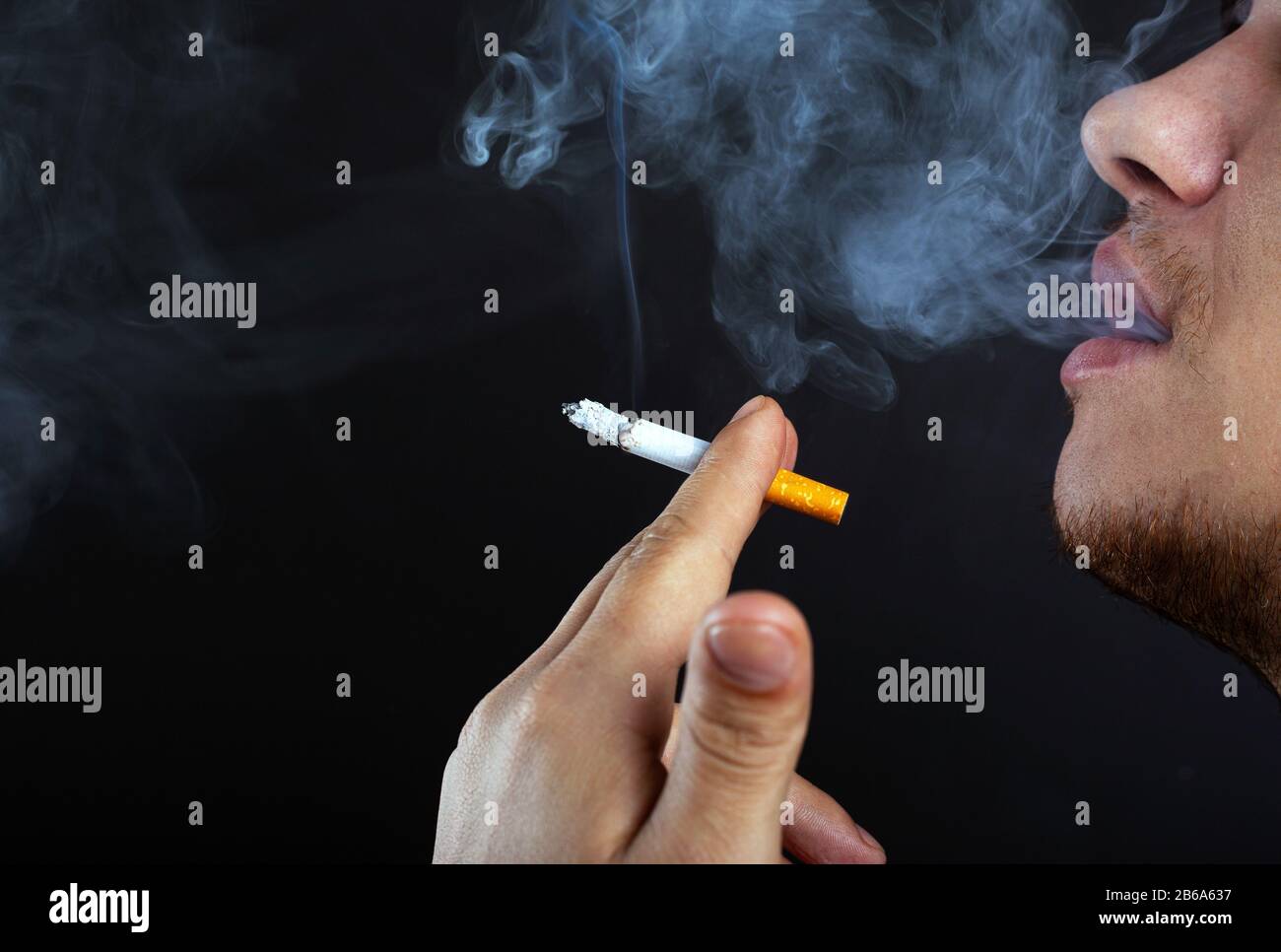 young man exhales smoke. harm from smoking cigarettes dark background close-up. Stock Photo