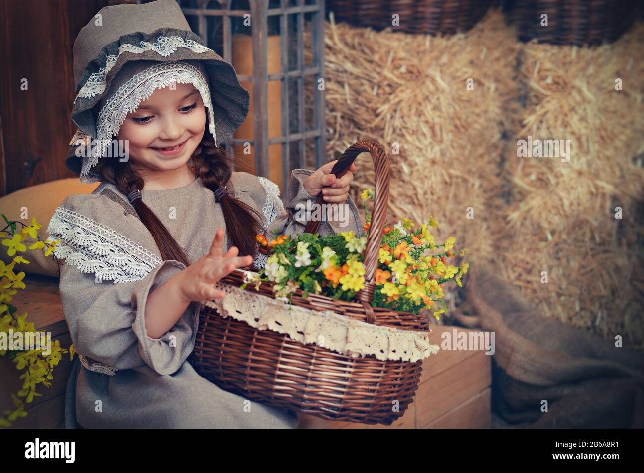 Beautiful girl in retro dress with a basket of flowers on a background of straw. Retro style. Easter card. Stock Photo