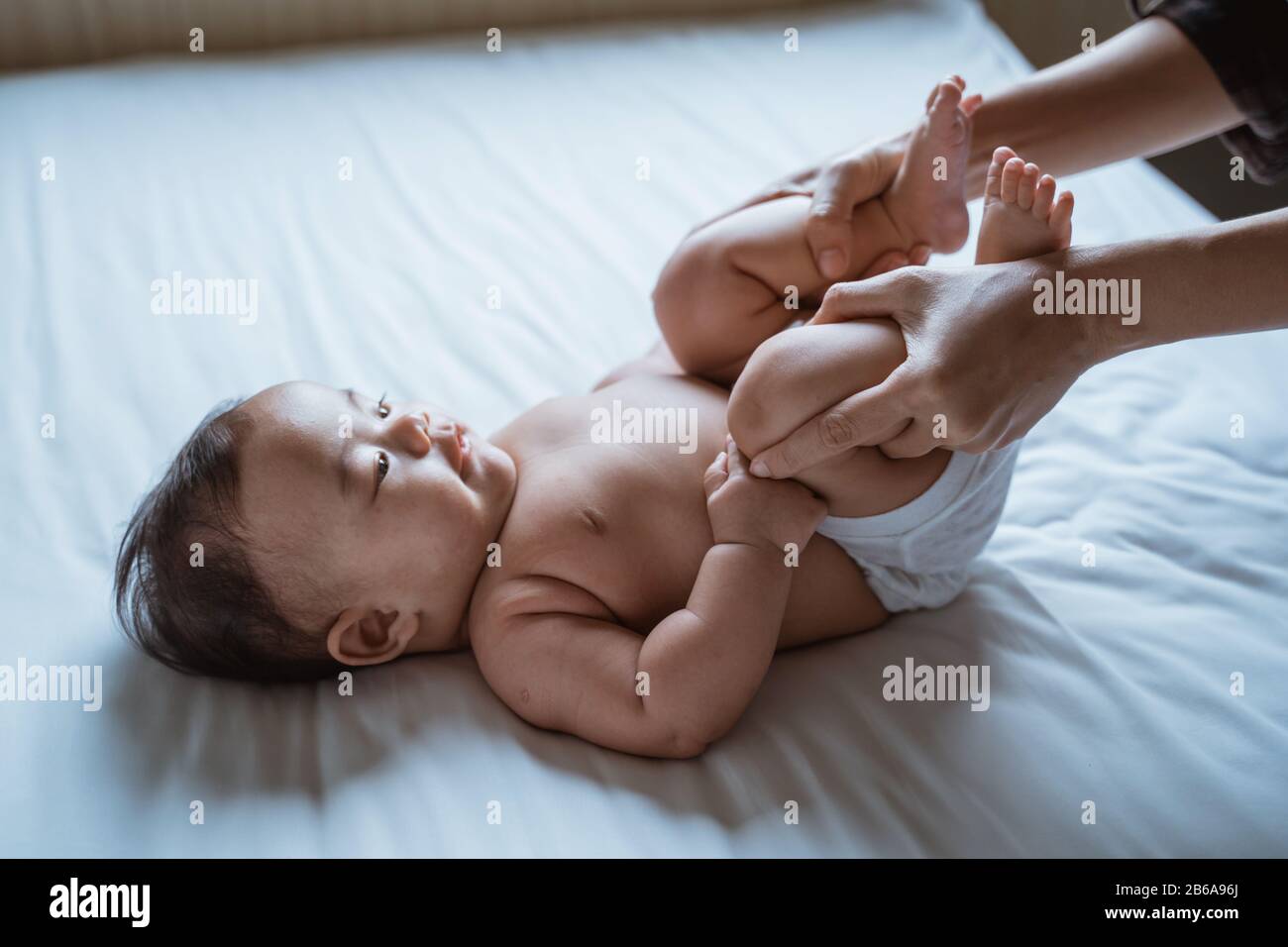 mother holds the feet of a baby child lying in bed giving massage Stock Photo
