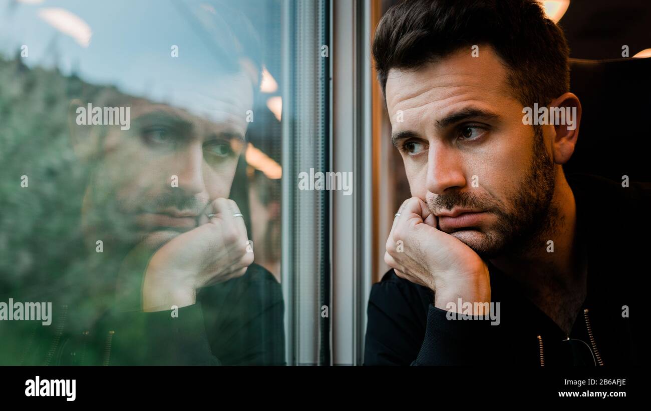 Young bearded man traveling by train in late afternoon Stock Photo