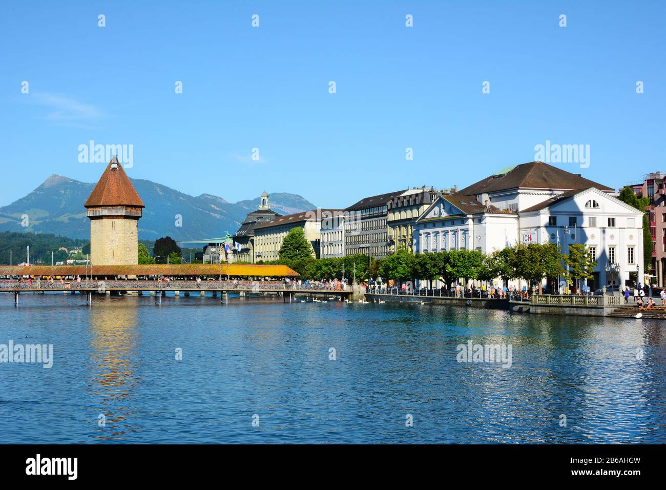 LUCERNE, SWITZERLAND - JULY 3, 2014: Chapel Bridge on the Reuss River. Mountains, Hotels and the train station are in the background. Stock Photo