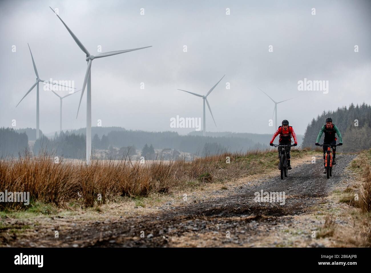 Two men ride mountain bikes in the shadow of wind turbines near Lluest-Wen Reservoir in South Wales. Stock Photo