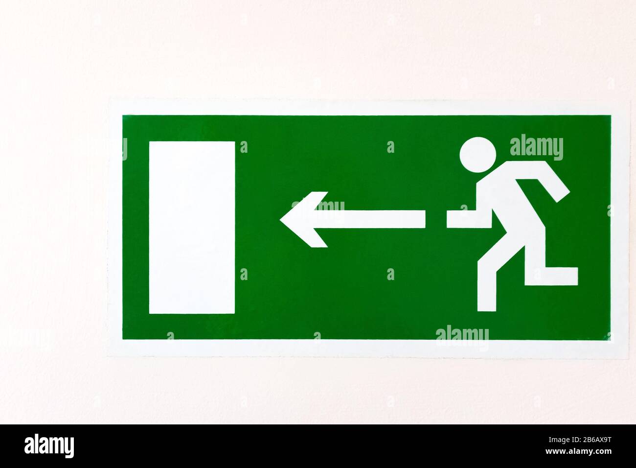 A green poster on a light wall. DIRECTION TO EVACUATION EXIT LEFT. Stock Photo