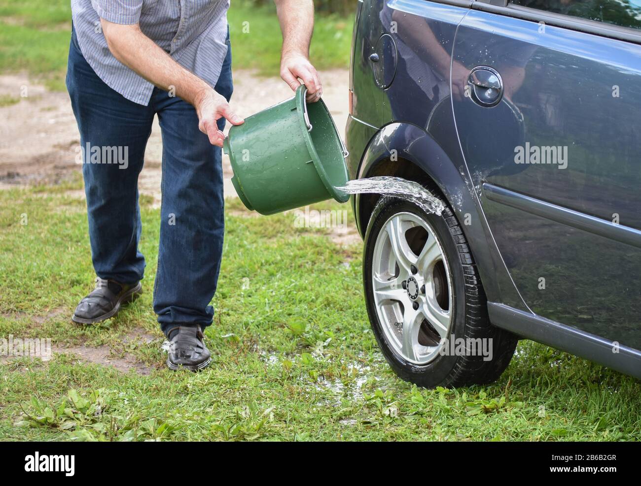 Man splashing water on a car with green bucket. Washing car Stock Photo